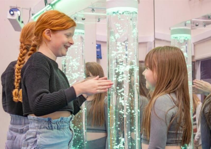 Two girls looking at a bubble tube and smiling
